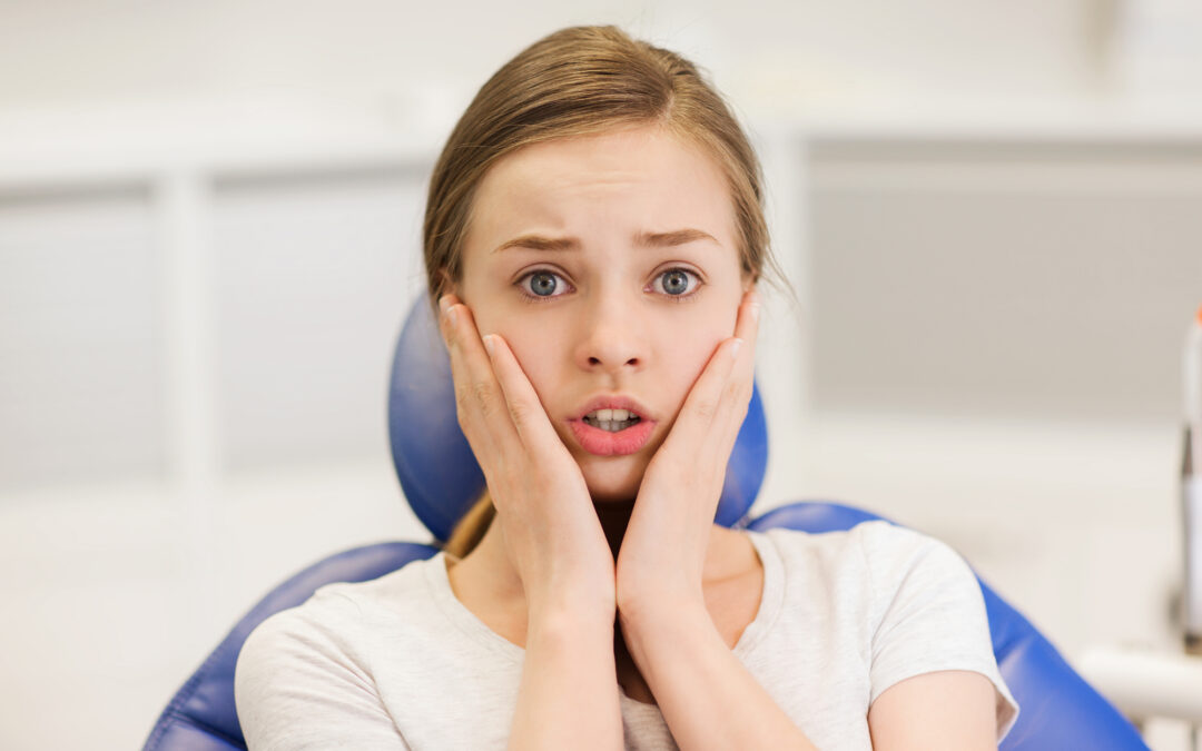 girl clutches her face while sitting in a dental chair to indicate the need for sedation dentistry