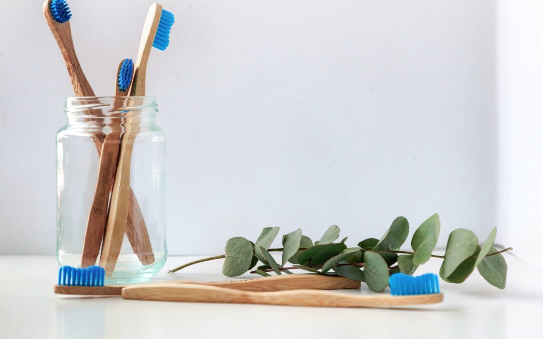 wooden toothbrushes in glass jar, eucalyptus, and toothbrushes on a white table
