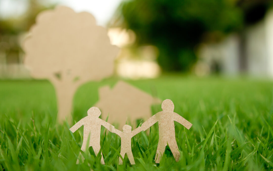 Paper cut of family with house and tree on fresh spring green grass