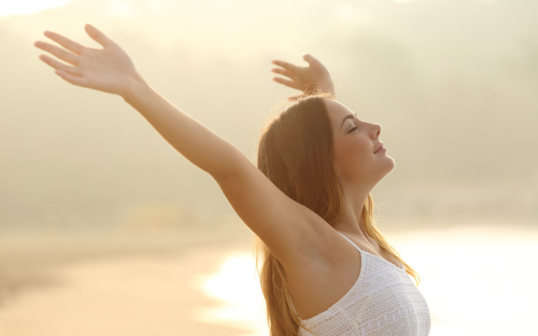 Relaxed woman breathing fresh air raising arms at sunrise with a warmth golden background
