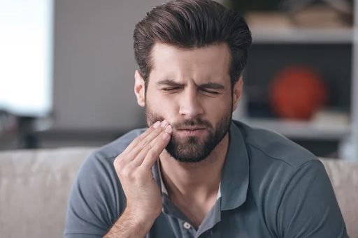 A man holds his hand to his face, wincing in pain from major cavities.