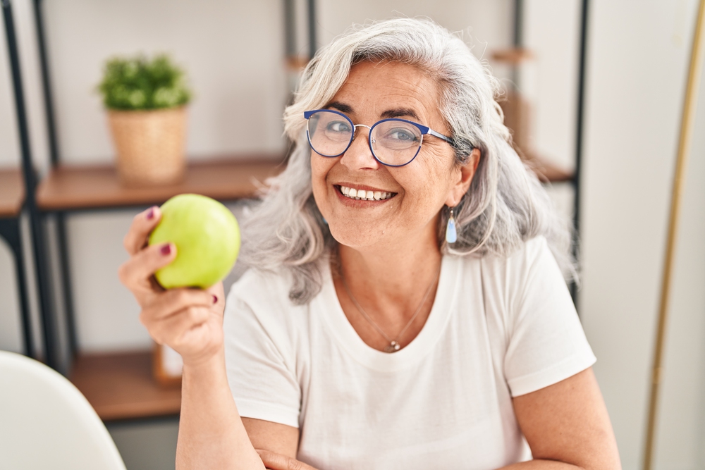 older woman with dental implants holding an apple