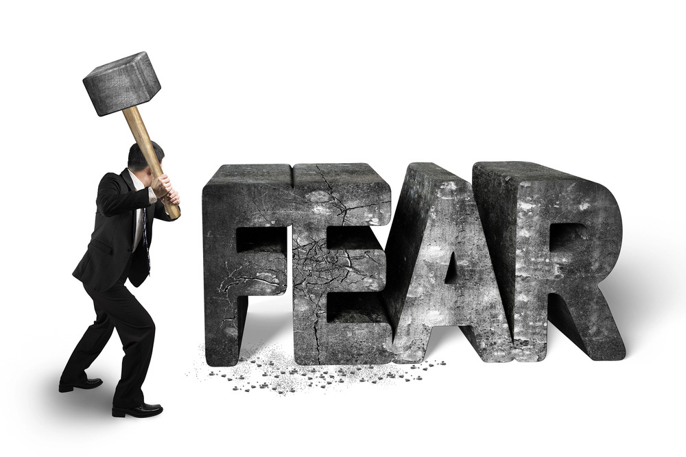 man in a suit using a sledge hammer to smash the word "FEAR"