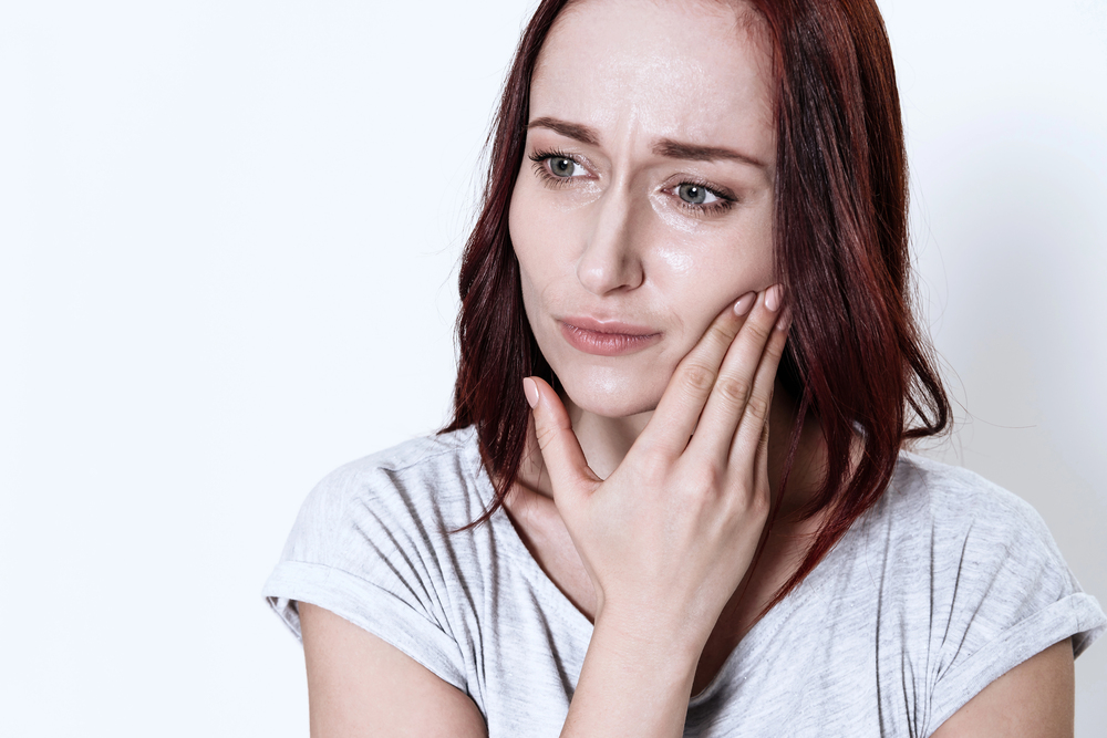 woman with brown hair in white shirt touching jaw