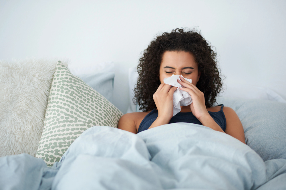 woman with COVID sitting in bed blowing her nose