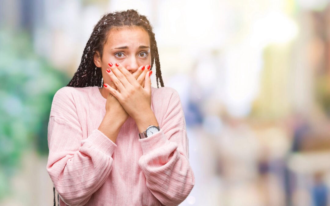 Young woman in pink sweater covers her mouth with both hands, indicating her fear about a first time dental office visit