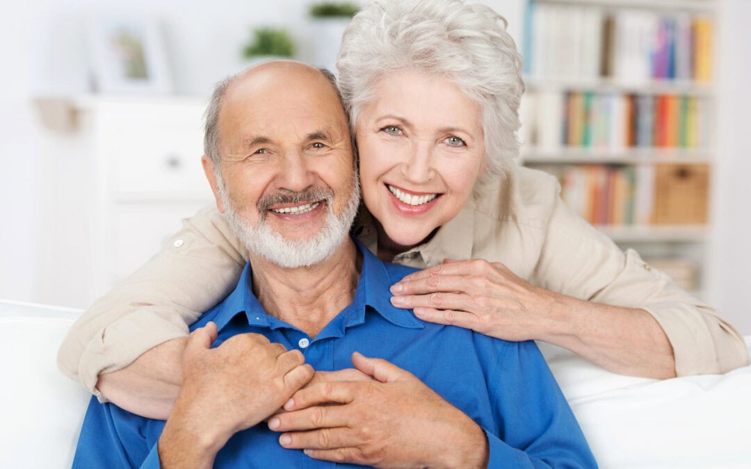 An affectionate white older coulple embrace and smile, showing off their beautiful, white veneers.