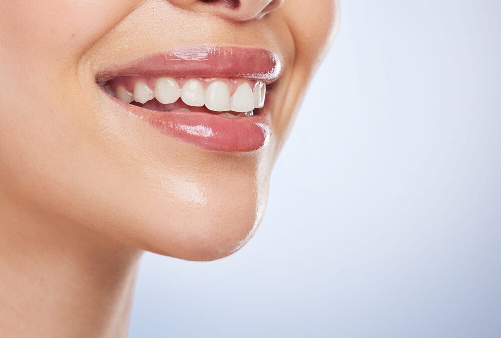 Close-up of a smiling person showing white teeth and glossy pink lips.