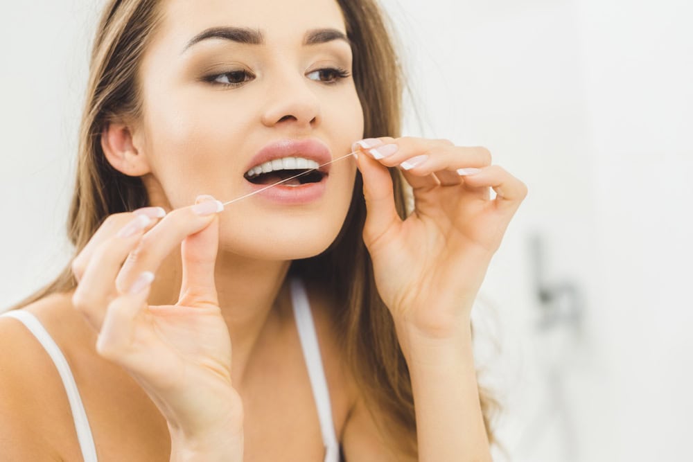 Smiling woman flossing her teeth to help prevent gum disease
